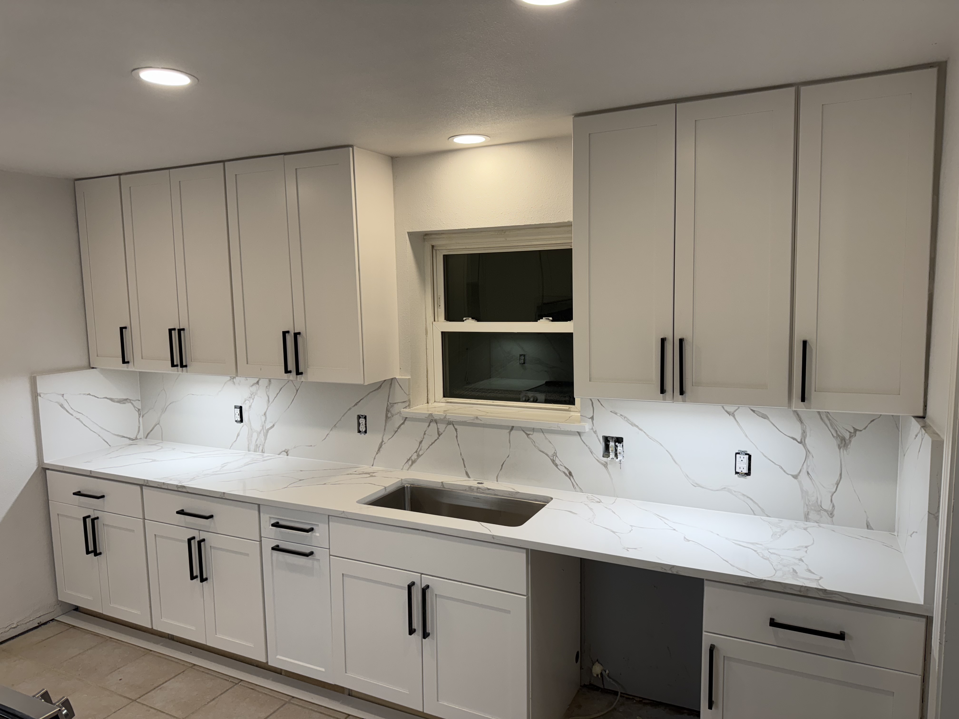 Remodeled kitchen with white shaker cabinets and marble backsplash